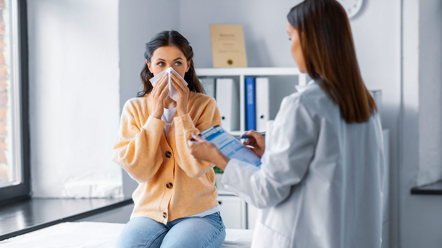 Eine Frau mit Grippe wird von einem Arzt untersucht.