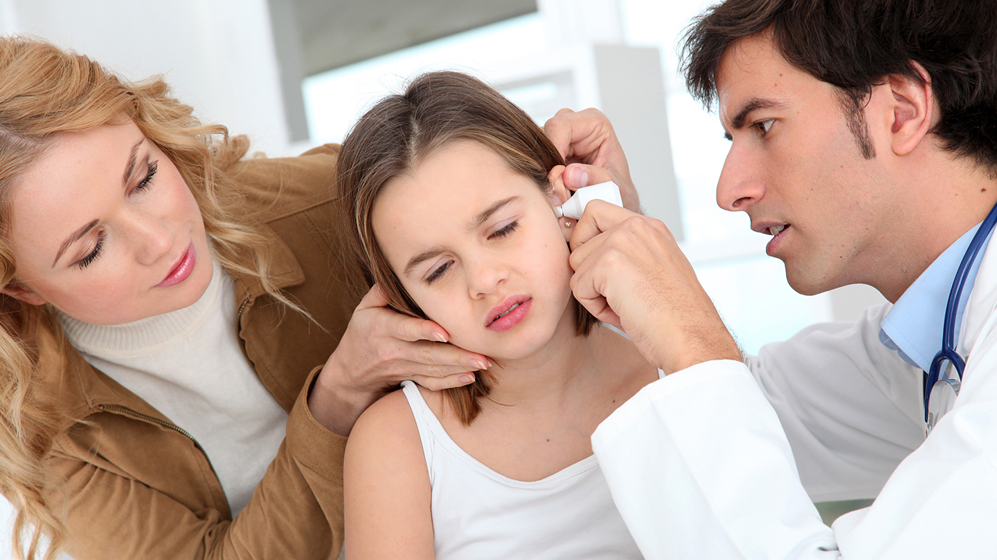 Der Arzt untersucht das Ohr des Mädchens; es handelt sich um eine Ohrenentzündung.
